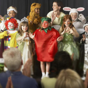 Children (4-9) wearing costumes and teacher waving on stage